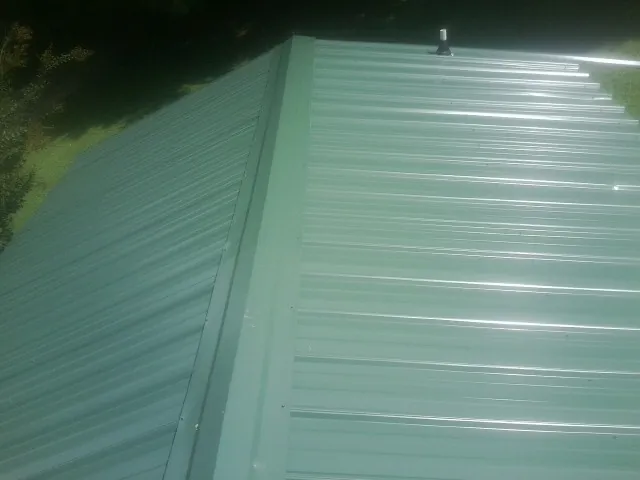 New green metal panels meeting at the ridge of a roof — Flat Roof Repair work by our crew in Cottage Grove
