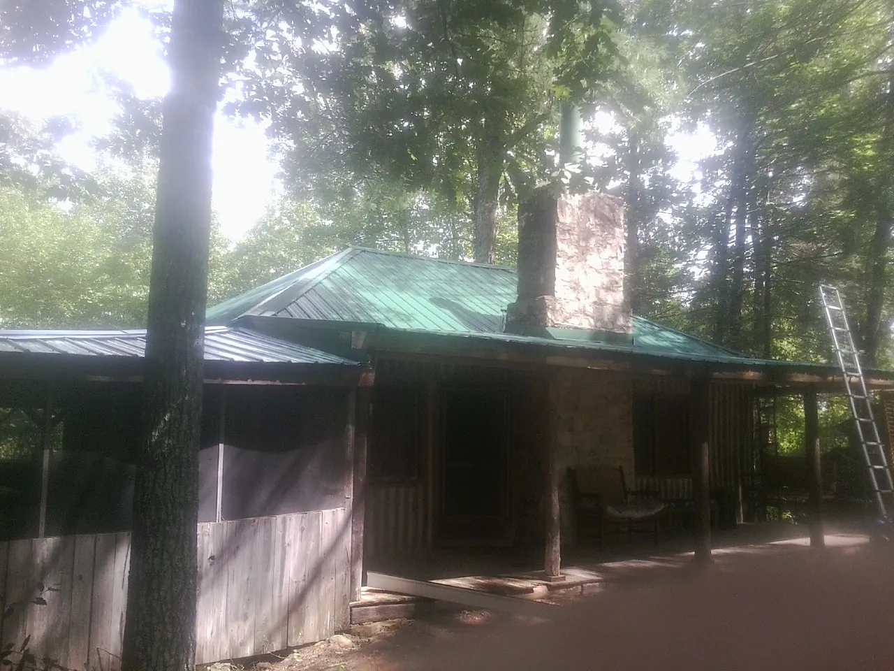 Green metal roof and stone chimney above a log cabin porch in Cottage Grove