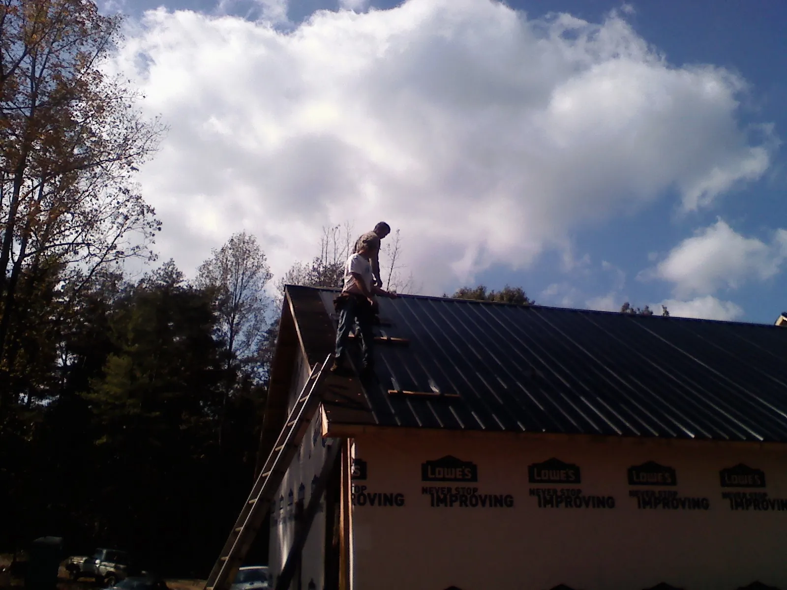 Roofer fastening dark metal panels high against a cloudy sky, from a Roof Inspection job in Cottage Grove